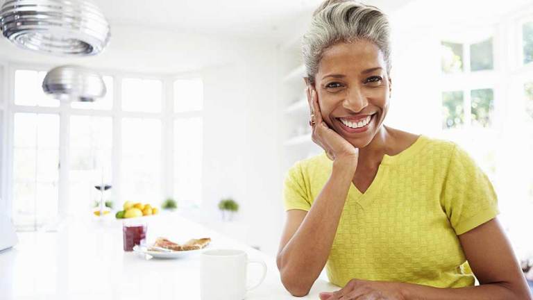 middle aged woman smiles at camera with chin on hand
