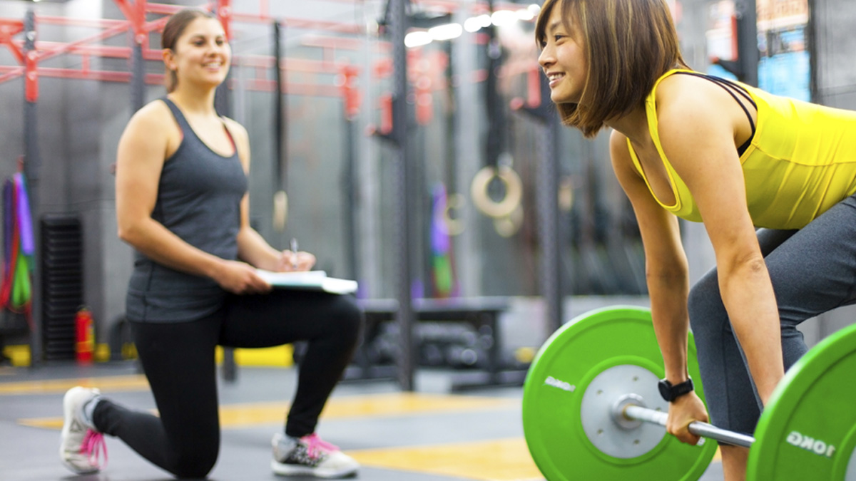 female personal trainer and young woman lifting weights