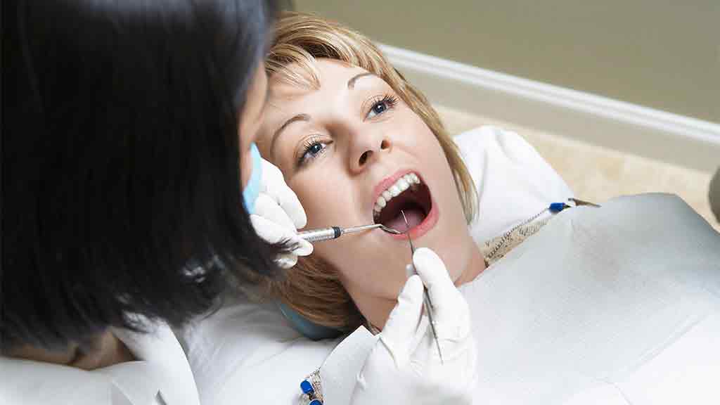 dentist performs dental work on woman in chair