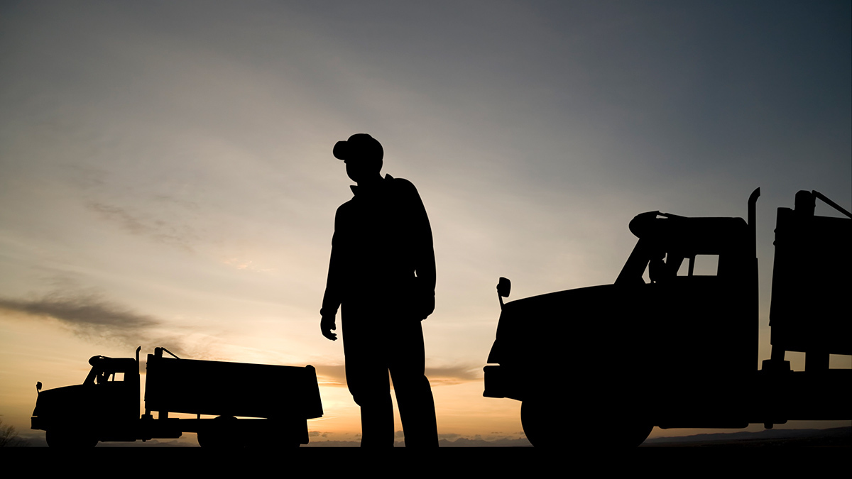 truck driver standing beside his truck in shadow
