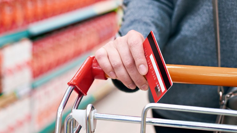 hand holding credit card while pushing shopping trolley
