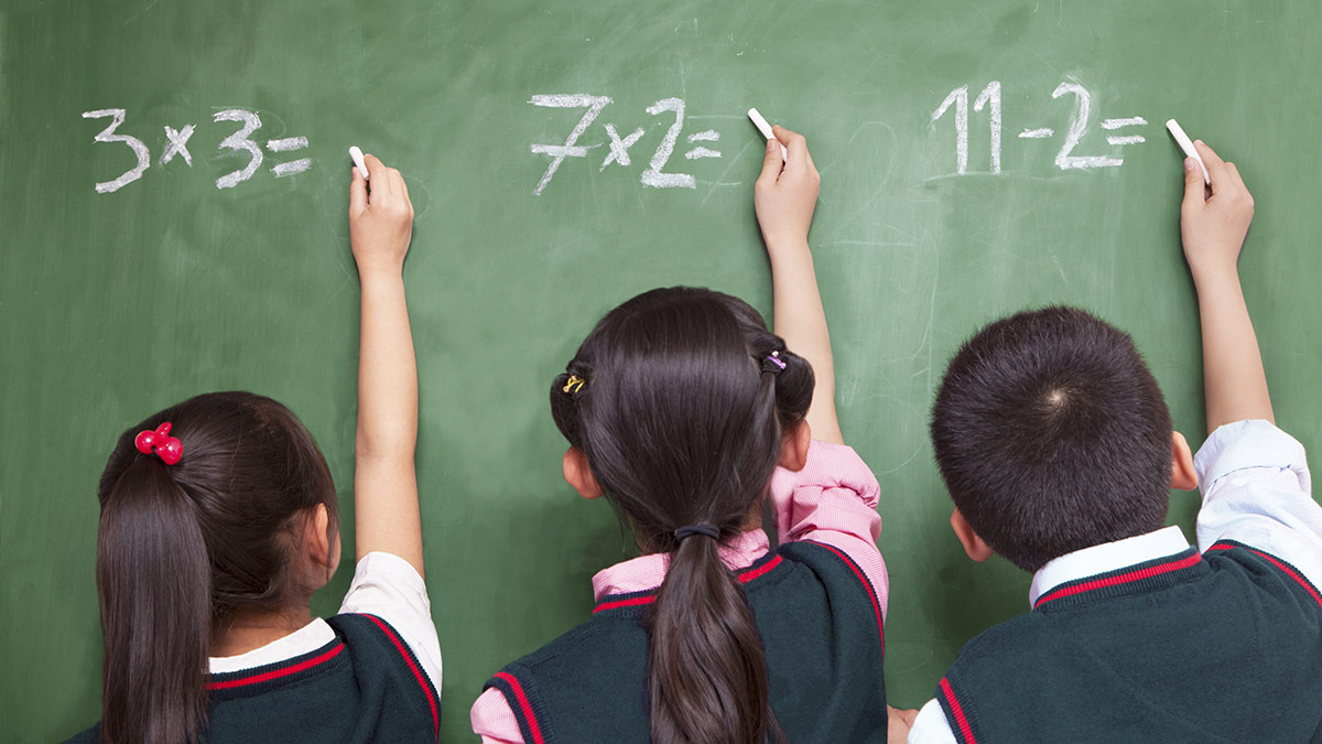 Three young students doing maths problems on a blackboard