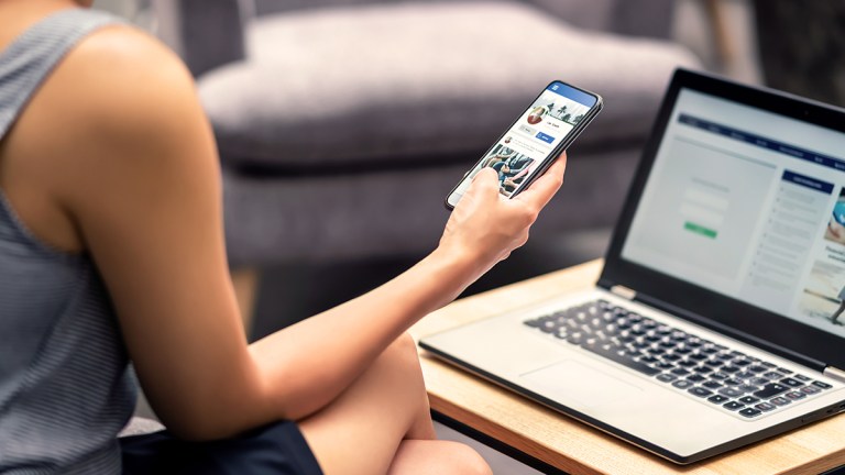 person_with_laptop_checking_social_media_on_smartphone