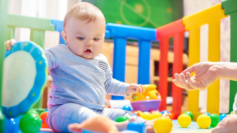baby sitting in a colourful playpen