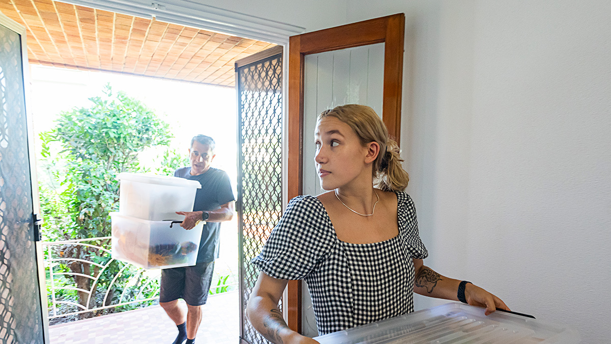 two_family_members_carrying_storage_boxes_into_rented_home