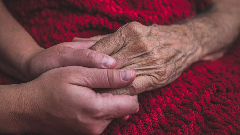 younger persons hand holding older persons hand