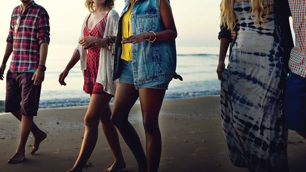 close-up of group of friends walking along beach