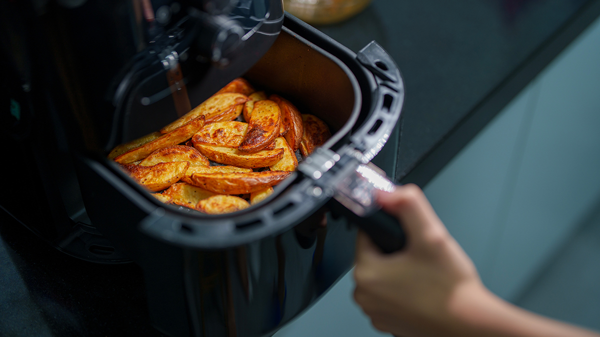 person removing air fryer basket with potato wedges to give it a shake