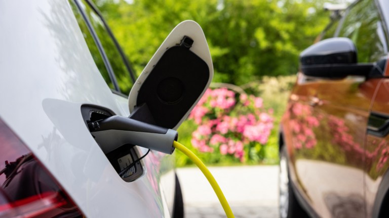 Close up of two parked cars with one plugged in to electric vehicle charger on the street
